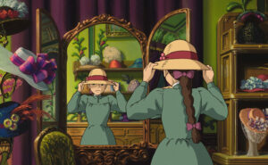Sophie, the main character from Studio Ghibli’s “Howl’s Moving Castle,” stands in front of a mirror adjusting a wide-brimmed hat with a red ribbon and flower. She wears a green dress with a long braid tied in a pink bow, surrounded by vibrant hats and rich decor in her hat shop.
